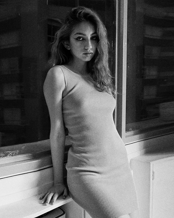 Fotografía en blanco y negro de una modelo con gabán y botas largas, en un ascensor.